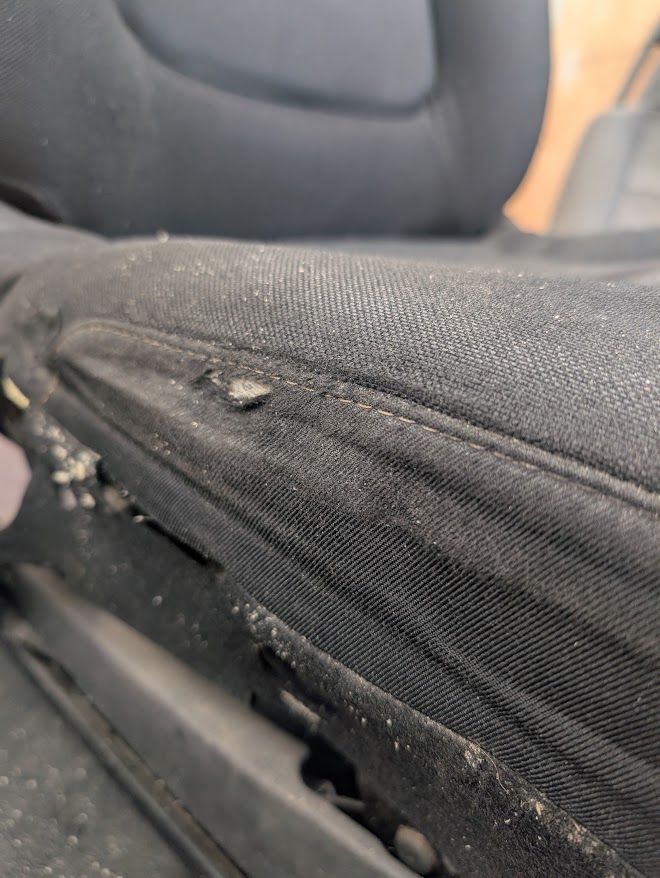 Black cloth vehicle seat before repair with wear and a hole in the bolster