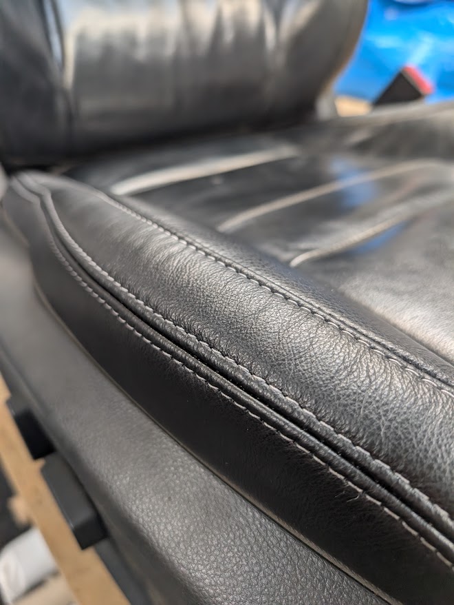 Vehicle seat bolster after repair with restored black leather and stitching